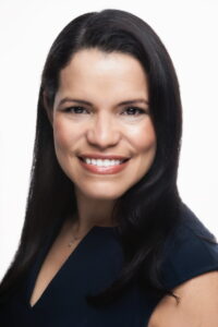 Confident professional woman with dark hair smiling, wearing a navy blazer for corporate or business profile.