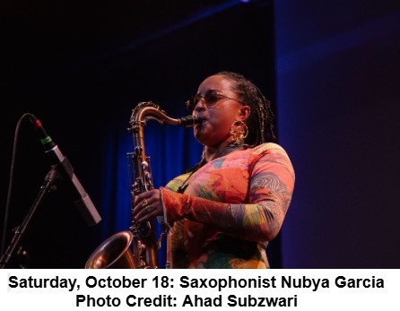 A woman plays a saxophone on stage under blue lighting. She wears glasses, large earrings, and a colorful long-sleeve shirt. Text below reads: Saturday, October 18: Saxophonist Nubya Garcia. Photo Credit: Ahad Subzwari.
