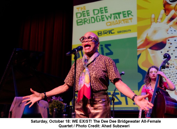 A female jazz singer wearing leopard print clothing, a colorful scarf, and large round glasses passionately performs on stage with a microphone. Behind her, a female musician plays a double bass. A large screen displays promotional text for "The Dee Dee Bridgewater Quartet" and "BRIC Brooklyn.