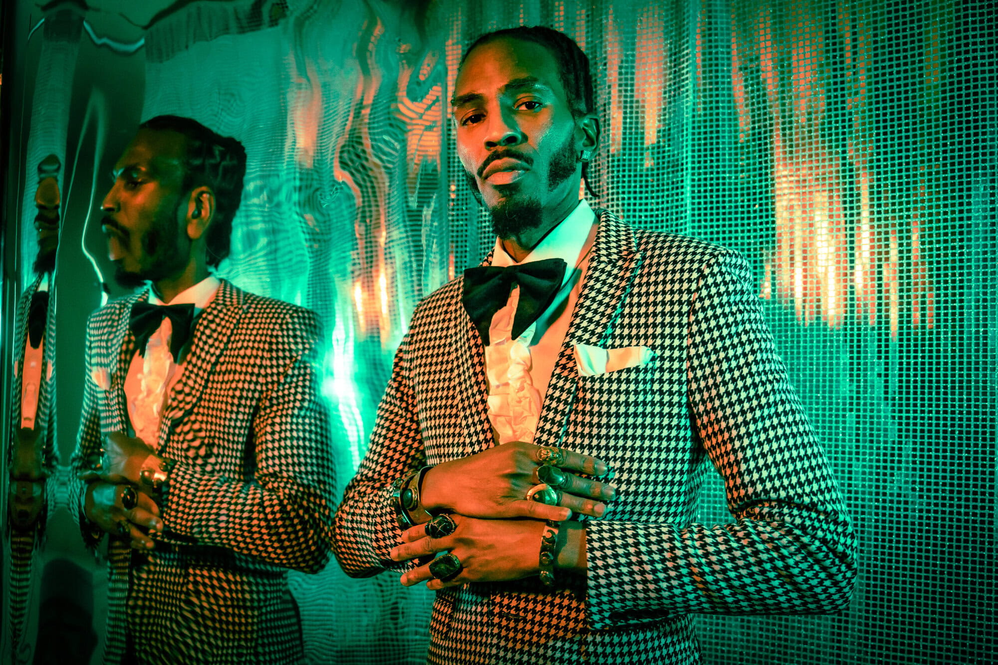 Elegant African man in a houndstooth patterned suit with bow tie, posing confidently at cultural event with reflective metallic background, showcasing fashion and diversity.